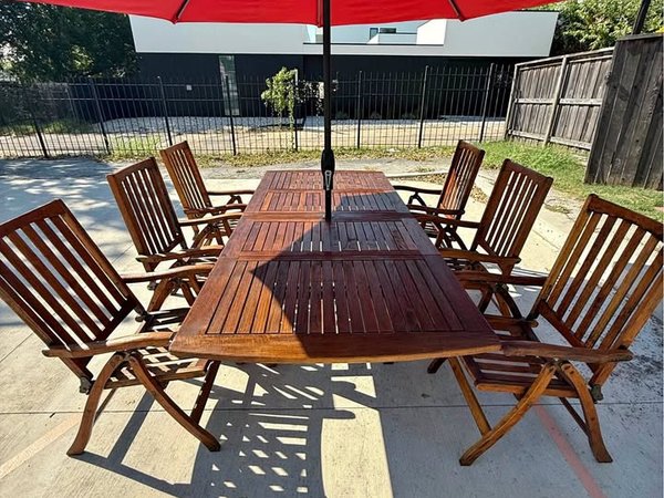 An image that captures the entire teak wood outdoor patio set with table, six chairs and a red umbrella.