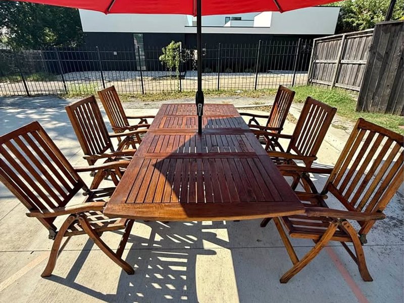 An image that captures the entire teak wood outdoor patio set with table, six chairs and a red umbrella.